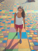 A young woman walks on pavement that is painted in different colors.