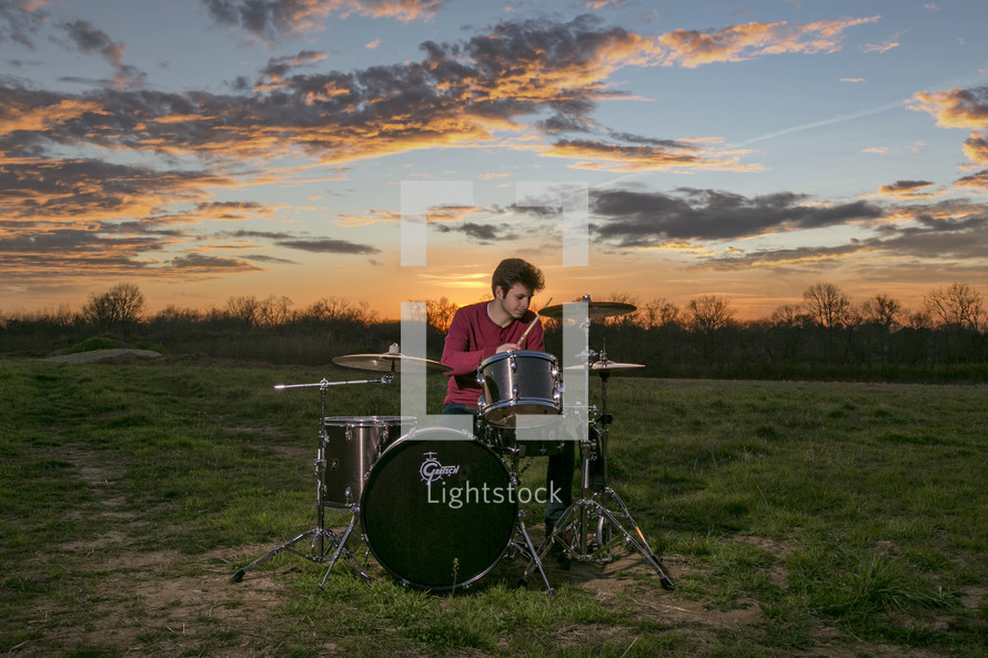 a man playing drums in a field at sunset 