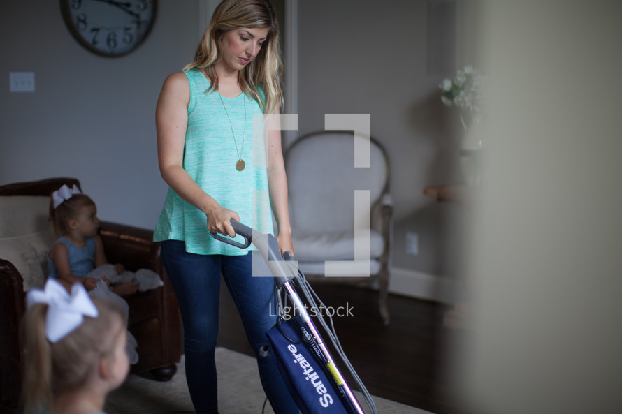 a woman vacuuming while her children watch tv 
