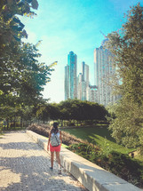 A woman walking on a brick walkway in a park near a big city.