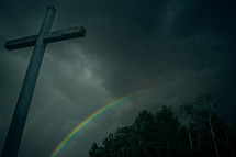 a gray cross and a rainbow in the sky