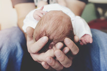 a father's hands cradling a newborn baby 