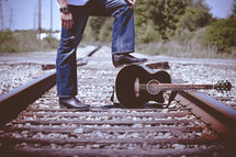 a man with a guitar standing on train tracks 