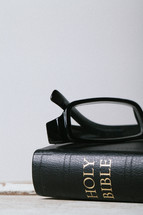 Reading glasses on top of closed Bible laying on wooden table.
