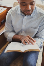 man reading a Bible sitting in a chair 