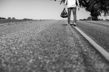 man standing in the middle of a road with his back to the camera holding a bag