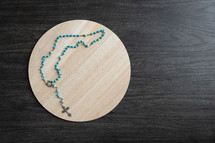 Blue rosary on a round wood tray with a dark background