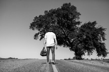 man standing in the middle of a road with his back to the camera holding a bag