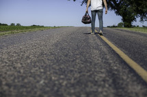 man standing in the middle of a road holding a bag