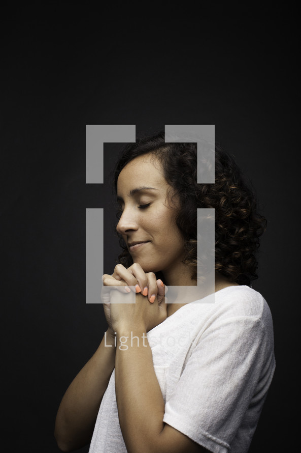 a side profile of a praying teen girl against a black background 