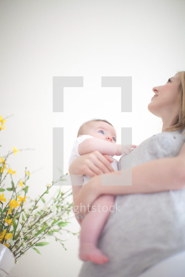 Mother holding infant daughter near vase of yellow flowers.