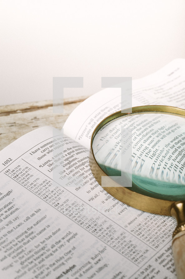 Magnifying glass on top of pages of open Bible.