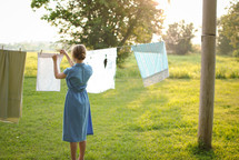 a woman hanging sheets on a clothesline 