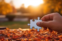 Hand holding jigsaw puzzle piece in autumn park. 