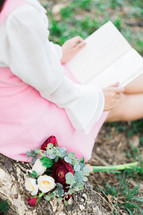 a girl sitting in the grass reading a book next to a bouquet of flowers 
