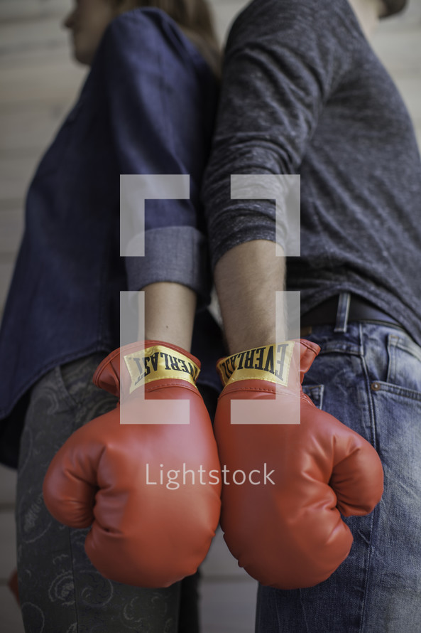 couple wearing boxing gloves standing back to back 