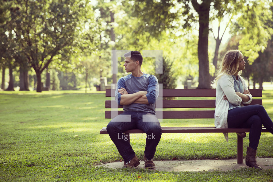 a fighting couple sitting on a park bench looking away from one another 