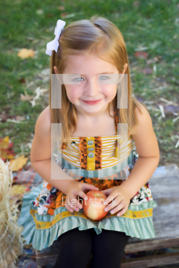 a smiling toddler girl holding an apple 