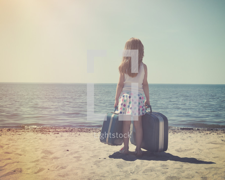 a little girl on a beach holding suitcases 