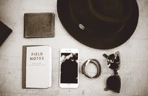 hair ties, sunglasses, wallet, field notes, notebook, table, cellphone, phone, hat