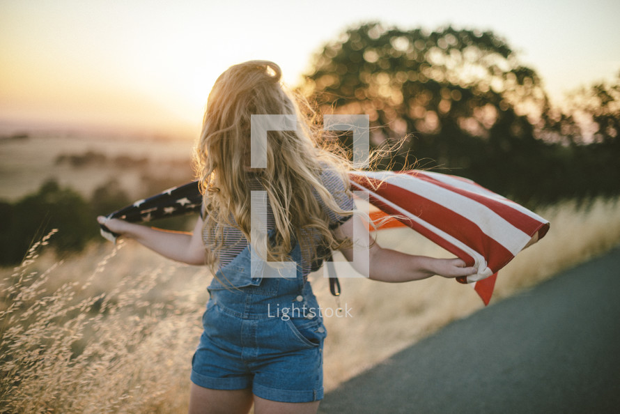 teen girl with an American flag in a field at sunset 