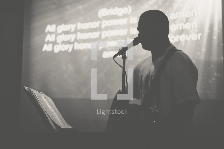 silhouette of a man singing into a microphone and lyrics on a projection screen 