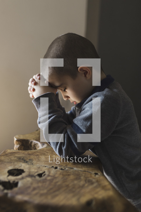 Little boy with his head down praying.