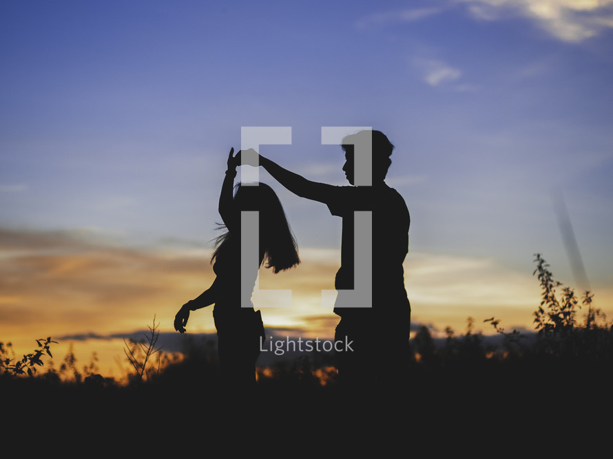 silhouette of a couple dancing holding hands at sunset 