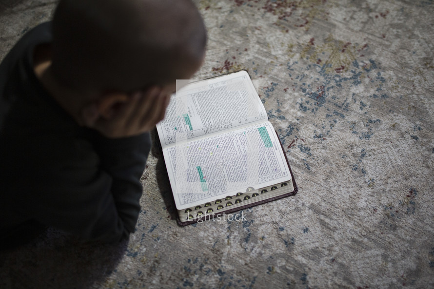 Little boy reading a Bible on the carpet.