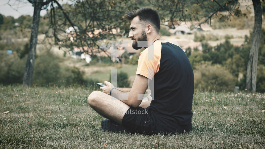a man sitting in a park holding his cellphone 