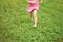 A girl in a pink dress running through a field of clover.