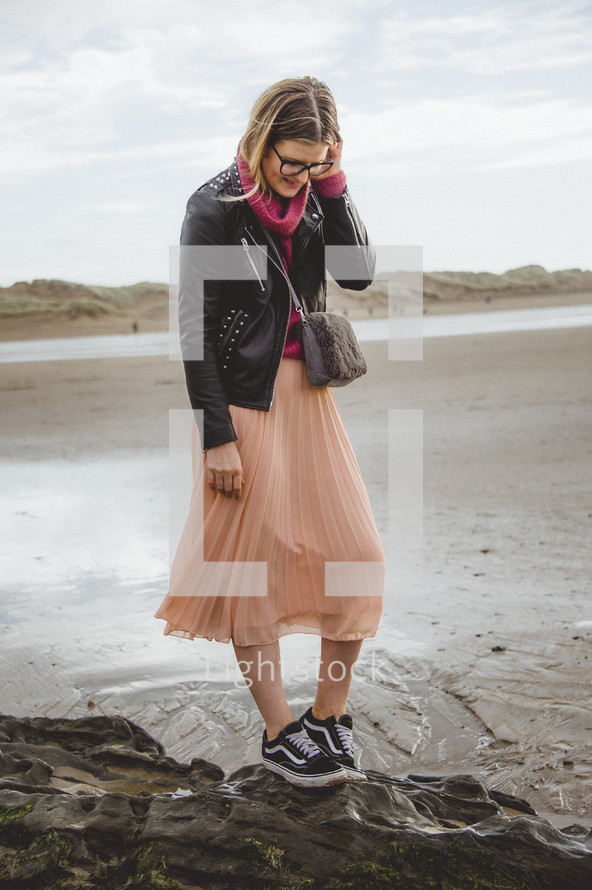 a woman in a skirt and sneakers walking on a beach 