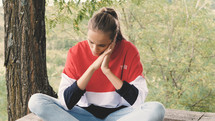 a young woman sitting outdoors praying 