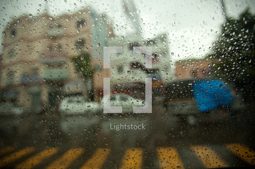 view of parked cars and a crosswalk through a wet window 