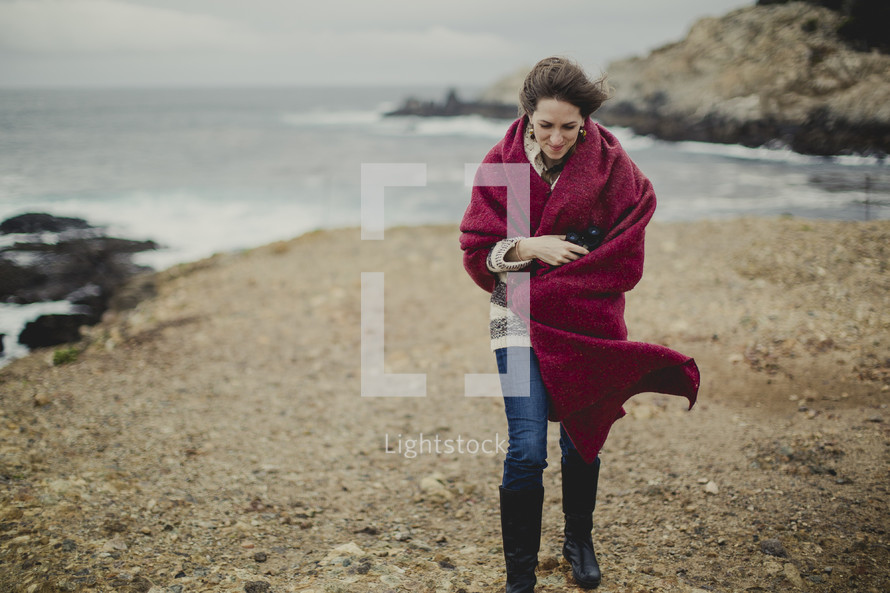 woman walking on a beach wrapped in a red blanket