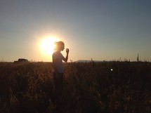man standing in a field under the glow of the setting sun 