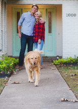 happy couple and their dog in front of their home 