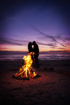 couple kissing on a beach behind at fire 