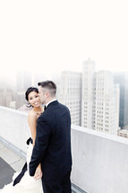 groom kissing his bride on the cheek on top of building in city fog wedding love romance marriage