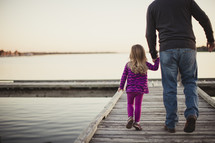 father holding hands with his daughter walking on a dock