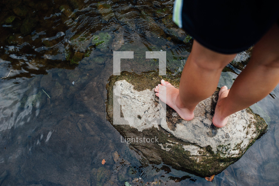 bare feet standing on a stone in a pond