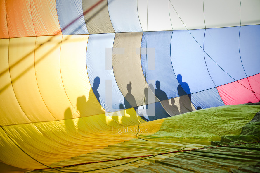 Onlookers cast shadows on the side of a hot air balloon.