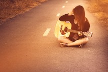 woman sitting in a road playing a guitar 