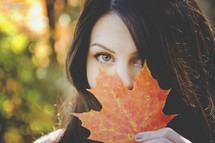 young woman covering her face with a fall leaf 