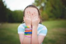a child covering her face with her hands 