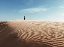 man standing at the top of a sand dune 