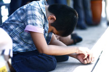 a boy kneeling with head bowed at a worship service 