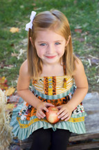 a smiling toddler girl holding an apple 