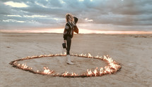 a female standing in a ring of fire in a desert 