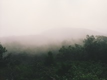 Silhouette of a mountain range through the fog over a meadow.